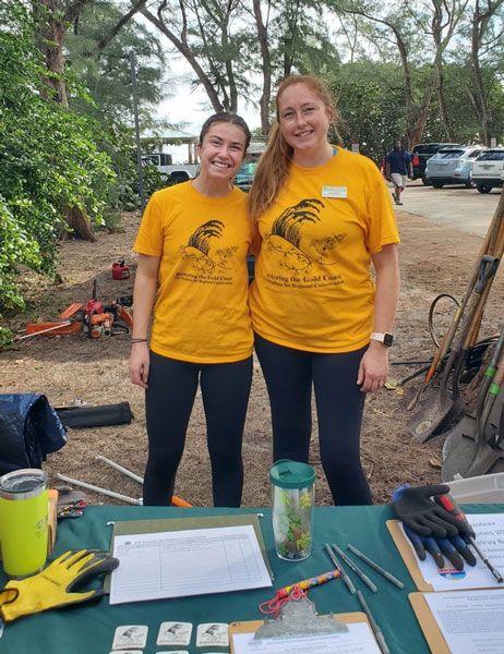 two young women in bright yellow-orange t-shirts in a wooded area