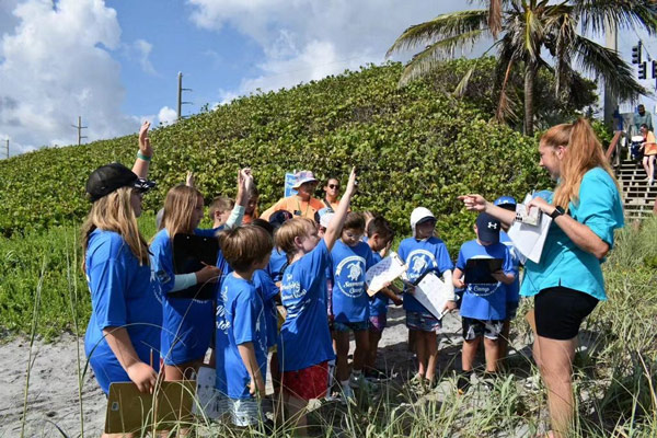 children in royal blue tee-shirts raise their hands to answer questions while standing on a dune